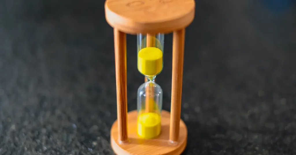 Wooden hourglass with yellow sand running out, illustrating the timing gap in ROAS vs CAC