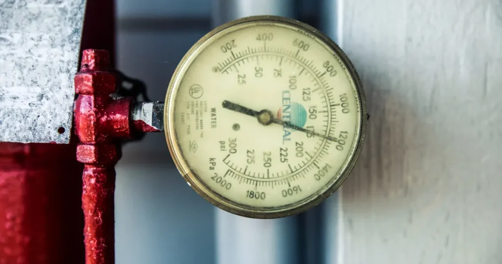 Close-up of an analog water pressure gauge on a red pipe, for a PPC audit