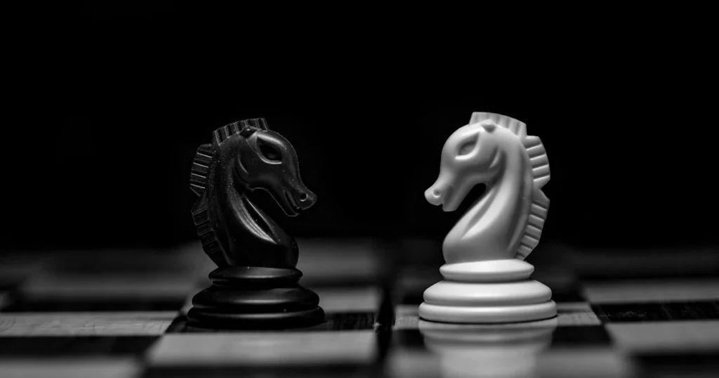 A black chess knight and a white chess knight facing each other on a board