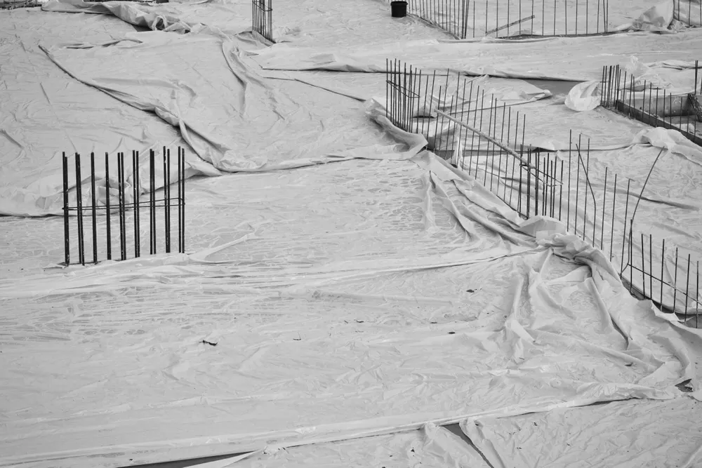 Construction site with foundations under protective sheeting and rebar standing upright