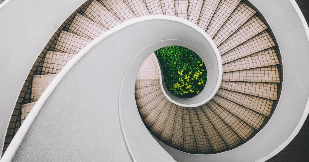 Top-down view of a white spiral staircase with tiled steps curling around a small garden