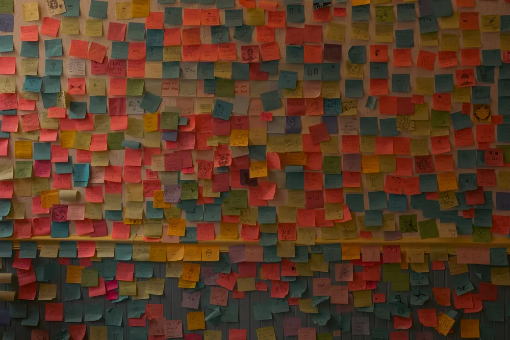 A wall covered in hundreds of colored sticky notes with hand-drawn doodles